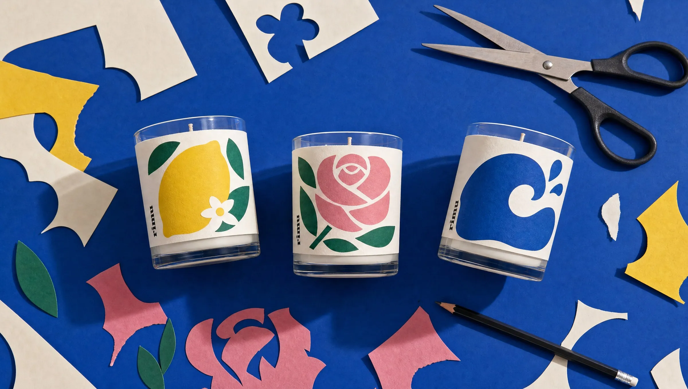 Three rimu candles on cobalt paper among scissors, a pencil and cut-paper scraps in cream, yellow, green and pink